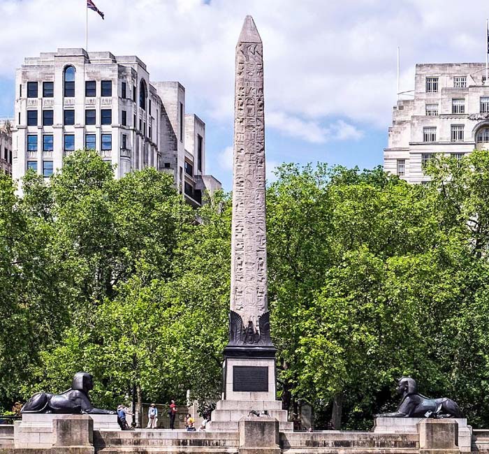Tall Egyptian obelisk with a sphinx on each side in London.